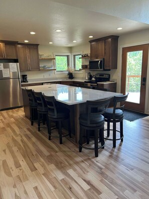 A modern kitchen with a large island, wooden cabinets, and a view of greenery outside. - Aces and Eights Lodge (Sturgis)