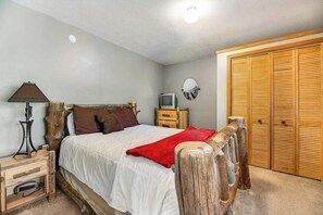 A bedroom with a bed, a wooden headboard, a nightstand, a lamp, a television, and a wardrobe. - Aces and Eights Lodge (Sturgis)