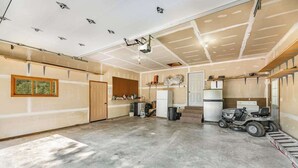 Eine geräumige Garage mit Betonboden, Deckenbeleuchtung und einer großen Tür, ein Fahrzeug steht in der Ecke.