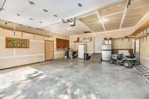 A spacious garage with a concrete floor, a ceiling with recessed lighting, a large door, and a vehicle parked in the corner. - Aces and Eights Lodge (Sturgis)