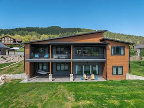 A modern two-story house with a balcony, large windows, and a well-maintained lawn. - The 19th Hole - Golf Simulator Home • Hot Tub & Views (Sturgis)