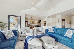 A modern living room with a sofa set, ottoman, and a view of the kitchen. - The 19th Hole - Golf Simulator Home • Hot Tub & Views (Sturgis)