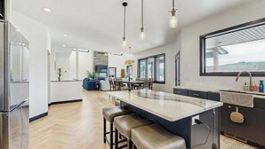 A modern kitchen with a large island, pendant lighting, and a view of the outdoors. - The 19th Hole - Golf Simulator Home • Hot Tub & Views (Sturgis)