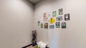A hallway with a golf bag and pillows, and a wall decorated with various golf-related signs. - The 19th Hole - Golf Simulator Home • Hot Tub & Views (Sturgis)