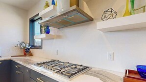 A modern kitchen with a gas stove, dark cabinets, and a window with a view. - The 19th Hole - Golf Simulator Home • Hot Tub & Views (Sturgis)