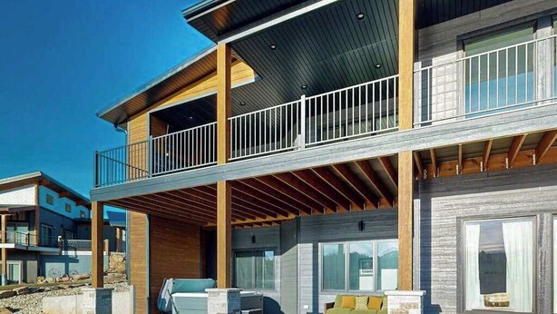 A modern two-story house with a balcony, large windows, and a covered outdoor seating area. - The 19th Hole - Golf Simulator Home • Hot Tub & Views (Sturgis)