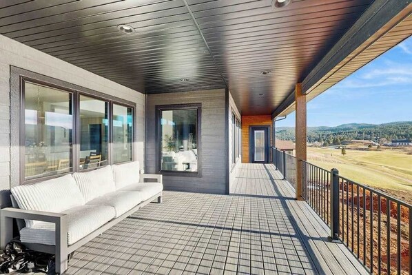A covered outdoor area with a wooden deck, a white sofa, and large windows. - The 19th Hole - Golf Simulator Home • Hot Tub & Views (Sturgis)