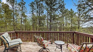 A wooden deck with two chairs and a table, surrounded by tall pine trees. - Boxelder Bluff - Secluded Home • Mountain Views (Rapid City)