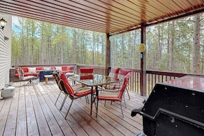 A covered outdoor deck with a table and chairs, a grill, and a view of a forest. - Boxelder Bluff - Secluded Home • Mountain Views (Rapid City)