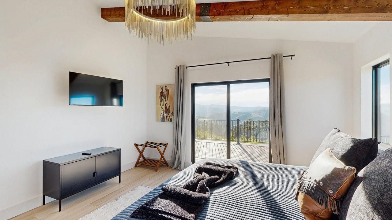 Une chambre moderne dotée d’un grand lit, d’un téléviseur à écran plat, d’un balcon avec vue et d’un plafond en bois.