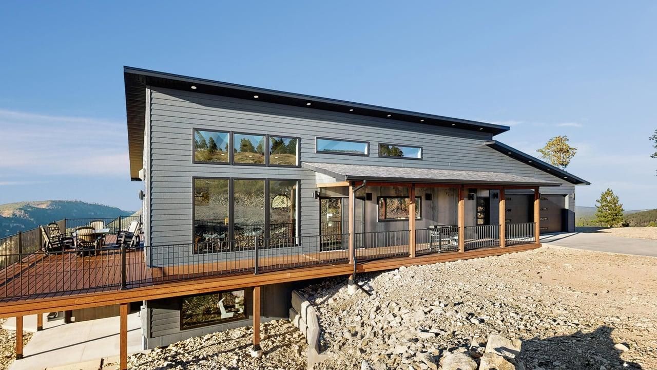 Een modern huis met twee verdiepingen, een terras, grote ramen en uitzicht op het omliggende landschap.