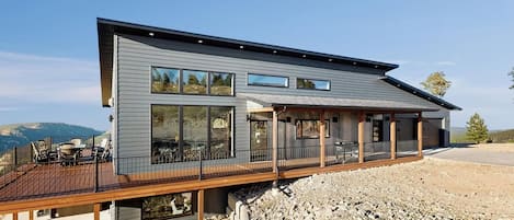Een modern huis met twee verdiepingen, een terras, grote ramen en uitzicht op het omliggende landschap.