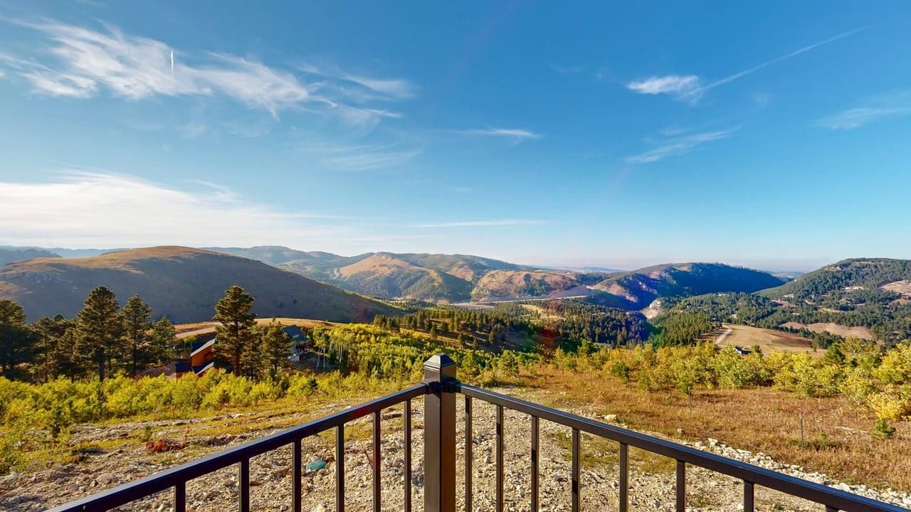 A mountainous landscape with a clear sky, a wooden railing, and a view of the valley below.
