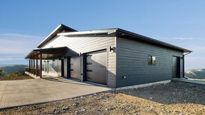Een modern gebouw met een garage, een overdekte veranda en uitzicht op het landschap.