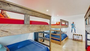 Ein Schlafraum mit Etagenbett, einem Holz-Kopfteil, einer roten und blauen Matratze sowie einem an der Wand befestigten Regal.