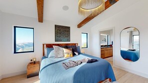 Een slaapkamer met een groot bed, een houten hoofdeinde, een nachtkastje, een spiegel en uitzicht op de omgeving.