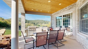 Un patio exterior con una parrilla, sillas y vistas a las montañas.