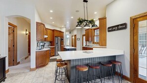 Una cocina moderna con armarios de madera, una isla central con taburetes y un cartel que dice 'cocina. canta. baila'.
