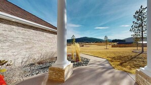 Um edifício com fachada de tijolos, uma coluna branca e um caminho pavimentado que leva a uma área gramada com árvores e uma paisagem montanhosa ao fundo.