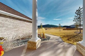 Ein Gebäude mit Backsteinfassade, einer weißen Säule und einer gepflasterten Auffahrt, die zu einer Grünfläche mit Bäumen und einer hügeligen Landschaft im Hintergrund führt.
