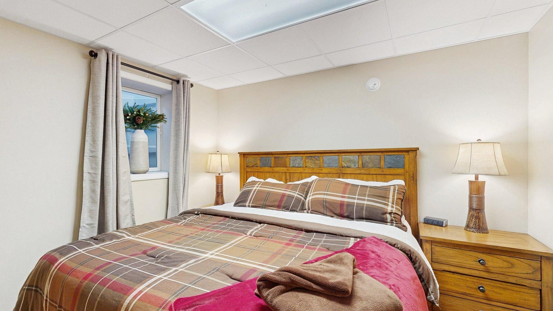 Une chambre à coucher avec un lit, des lampes de chevet, une table de chevet, une fenêtre avec des rideaux et un luminaire au plafond.
