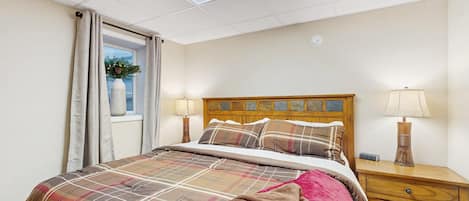 A bedroom with a bed, bedside lamps, a nightstand, a window with curtains, and a ceiling light.