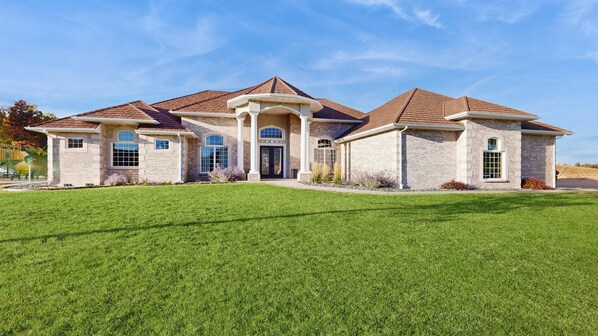 A two-story house with a brick facade, a central entrance with a decorative door, and a well-maintained lawn in front. - High Country Pool House - Private Indoor Pool • 2 Hot Tubs (Sturgis)