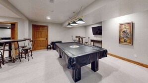 Quarto com mesa de bilhar, cadeiras, porta de madeira e um cartaz na parede.