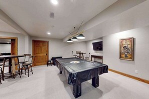Ein Zimmer mit Billardtisch, Stühlen, einer Holztür und einem Poster an der Wand.