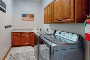 A laundry area with a front-loading washer and dryer, wooden cabinets, a herringbone-patterned rug, and a wall-mounted American flag.