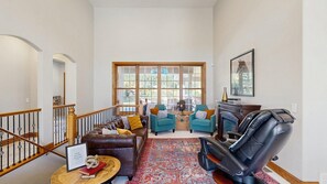 A spacious living area with a fireplace, leather armchair, and a large window offering a view of the outdoors. - High Country Pool House - Private Indoor Pool • 2 Hot Tubs (Sturgis)