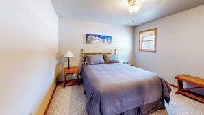 A bedroom with a bed, a nightstand, a lamp, a painting, a window, and a bench. - Hilltop Getaway - Hilltop Home • Hot Tub & Billiards (Lead)