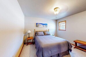 Quarto com cama, mesa de cabeceira, luminária, quadro, janela e um banco.