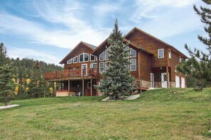 A two-story wooden house with a balcony, a covered porch, and a large evergreen tree in front. - Hilltop Getaway - Hilltop Home • Hot Tub & Billiards (Lead)