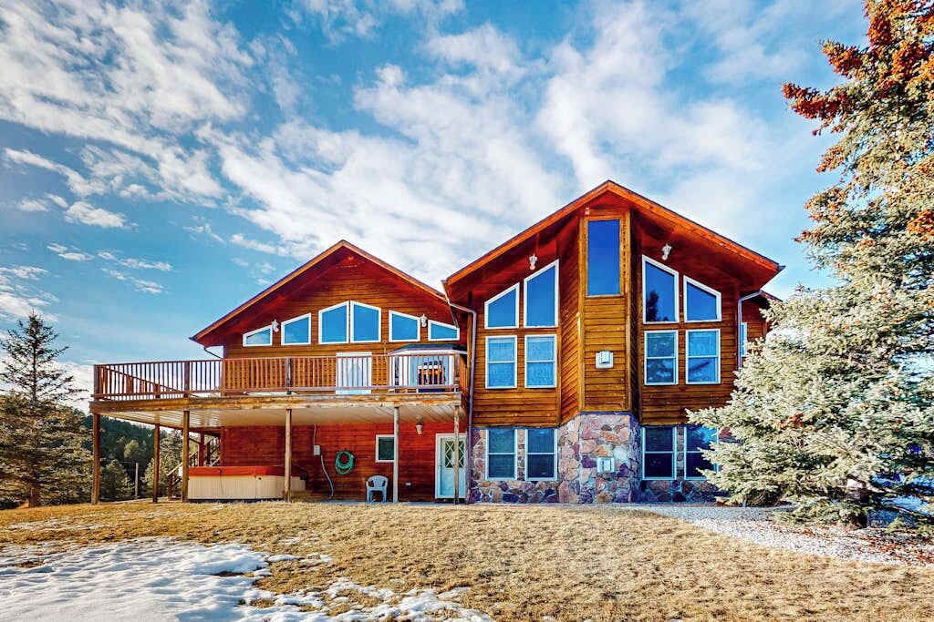 Une cabane en bois à deux étages, dotée d’un balcon, de grandes fenêtres et de fondations en pierre.