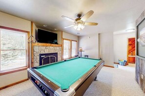 Ein Billardtisch in einem Raum mit Deckenventilator, Steinwand und einem darüber montierten Fernseher.