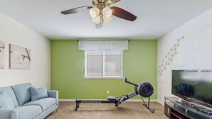 Ein Wohnzimmer mit Deckenventilator, Laufband, Fernseher und grüner Wand.