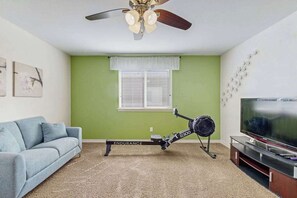 Ein Wohnzimmer mit Deckenventilator, Laufband, Fernseher und grüner Wand.