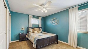 Ein Schlafzimmer mit Bett, Nachttisch, Lampe, Deckenventilator und einer geometrischen Wanddekoration.