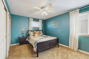 Ein Schlafzimmer mit Bett, Nachttisch, Lampe, Deckenventilator und einer geometrischen Wanddekoration.