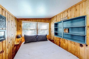 A room with wooden walls, a bed with white bedding, two bedside lamps, and a window with blinds. - Miller's Eden 1 - Woodsy Cabin • Views Near Pikes Peak (Green Mountain Falls)