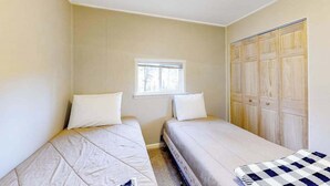 Ein Zimmer mit zwei Betten, einem Fenster und einem Holzschrank.