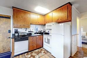 Eine kleine Küche mit Holzschränken, einem Geschirrspüler, einem Herd und einem Kühlschrank.