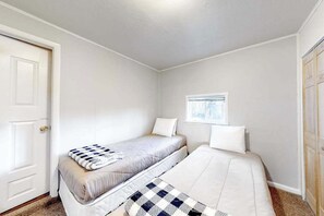 Ein Zimmer mit zwei Betten, einem Fenster und einer Tür.