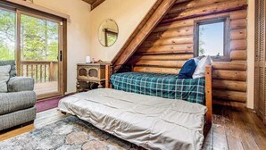 A log cabin bedroom with a bed, a chair, a small table, and a window. - Pikes Peak Retreat - Cabin w/ Pikes Peak & Forest Access (Divide)