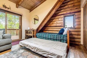 A log cabin bedroom with a bed, a chair, a small table, and a window. - Pikes Peak Retreat - Cabin w/ Pikes Peak & Forest Access (Divide)