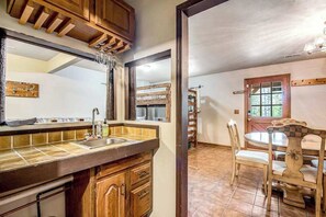 A kitchen with wooden cabinets, a sink, and a dining area with a table and chairs. - Pikes Peak Retreat - Cabin w/ Pikes Peak & Forest Access (Divide)