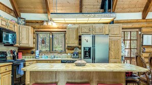 A kitchen with wooden cabinets, a central island with stools, a refrigerator, and a microwave. - Pikes Peak Retreat - Cabin w/ Pikes Peak & Forest Access (Divide)