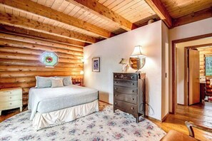 A bedroom with a wooden ceiling, a bed with a floral bedspread, a dresser, and a wall-mounted lamp. - Pikes Peak Retreat - Cabin w/ Pikes Peak & Forest Access (Divide)
