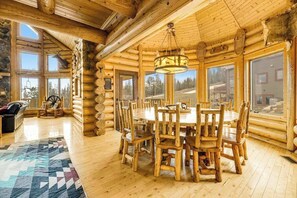 A log cabin interior with a central dining table surrounded by chairs, large windows, and a fireplace. - Liberty Lodge at Terry Peak - Ski-In/Ski-Out Lodge • Hot Tub (Lead)